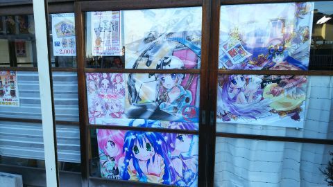 駄菓子屋さんの昔ながらの味のある店構えの引き戸には、様々なアニメのポスターが貼られています。